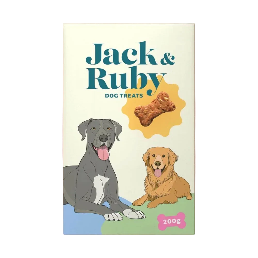A package of Jack & Ruby dog treats stands upright against a solid peach-pink background. The box is cream-colored with teal text, an illustration of a gray dog and a golden retriever, a bone treat graphic, and a pink bone-shaped label reading 200g.