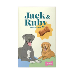 A package of Jack & Ruby dog treats stands upright against a solid peach-pink background. The box is cream-colored with teal text, an illustration of a gray dog and a golden retriever, a bone treat graphic, and a pink bone-shaped label reading 200g.